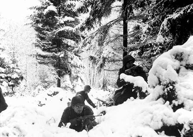 soldiers crouched behind snow covered trees in Belgium during world war 2