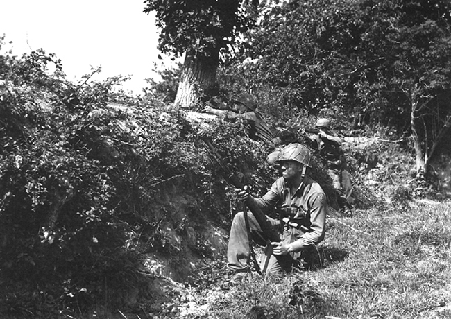 soldiers crouched behind hedgerows in France during world war 2