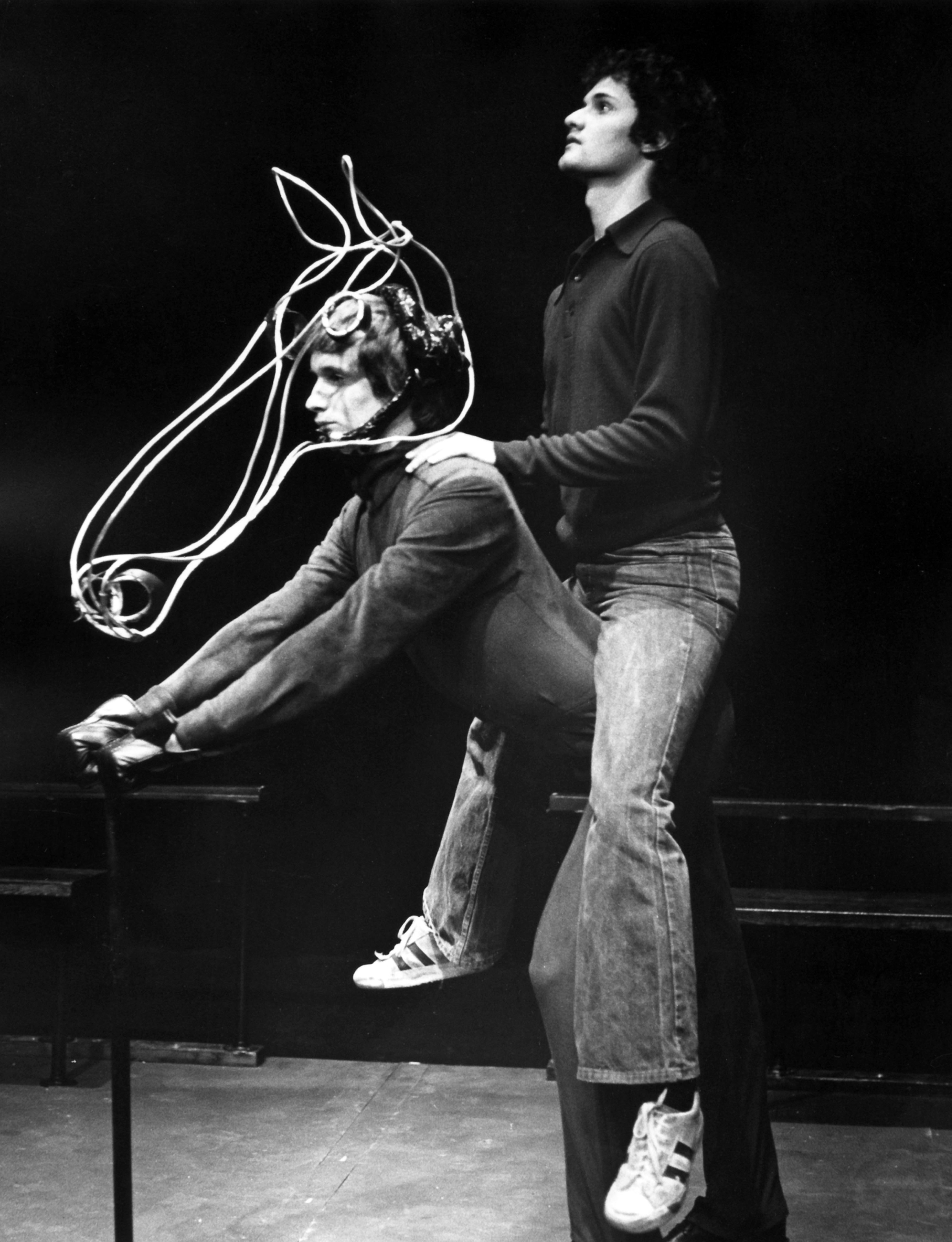 black and white photograph of two people in theatrical production, one person portraying a horse while the other person sits on their back