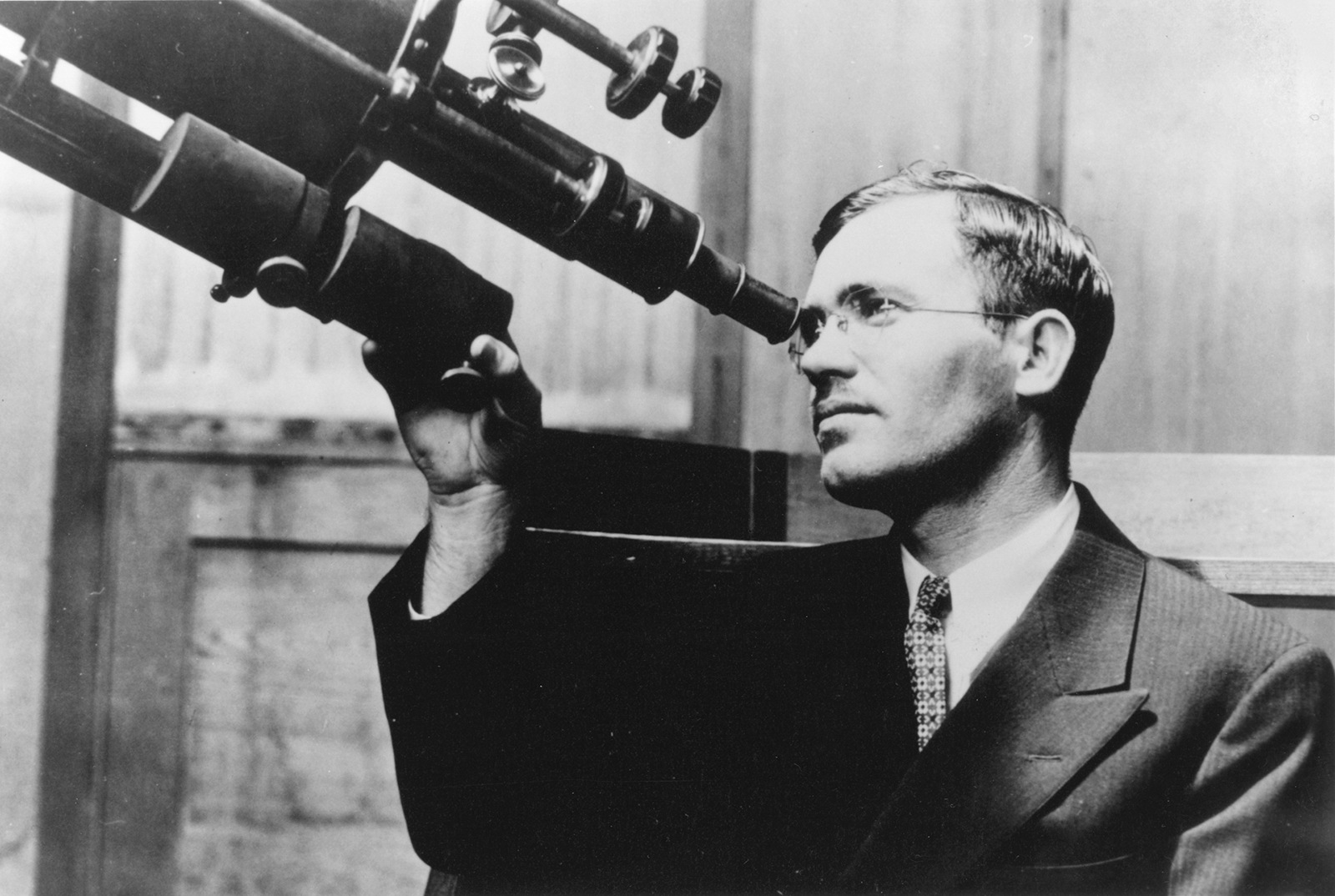 black and white portrait of Clyde Tombaugh looking through telescope