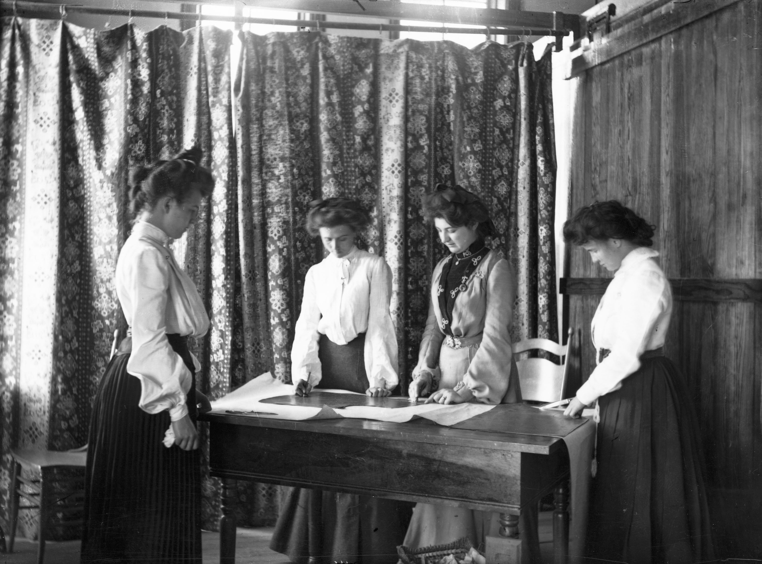 black and white photograph of women standing around a table, circa early 1900s